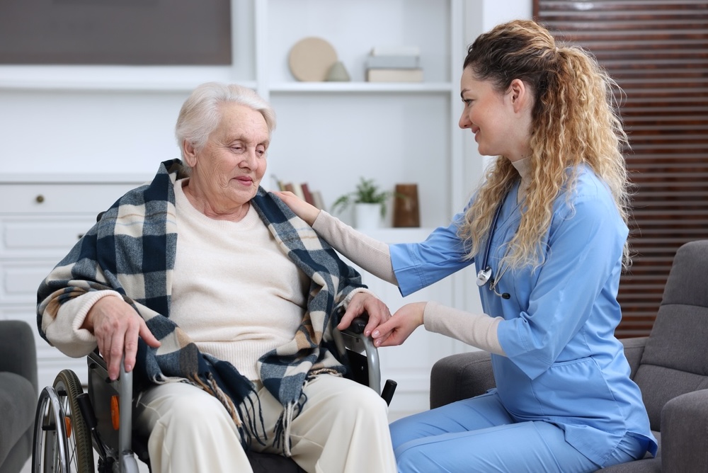 Care worker supporting senior woman in wheelchair indoors